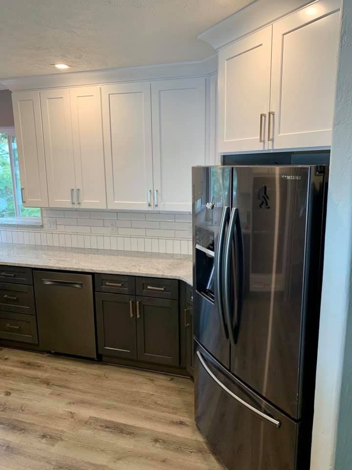 Kitchen with white upper cabinets, dark gray lower cabinets, stainless steel refrigerator, and light countertops.