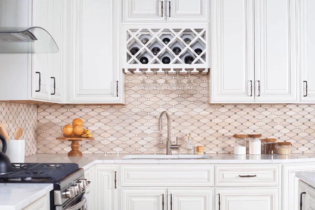 White kitchen with wine rack, marble backsplash, and fruit on a wooden stand.