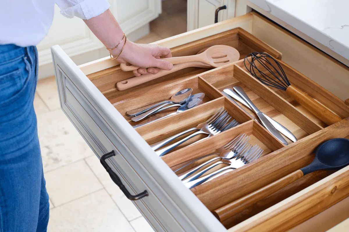 Person reaching into a kitchen drawer filled with utensils.