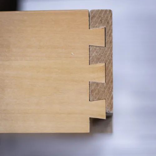 Close-up of a dovetail joint connecting two pieces of light-colored wood, showcasing construction.
