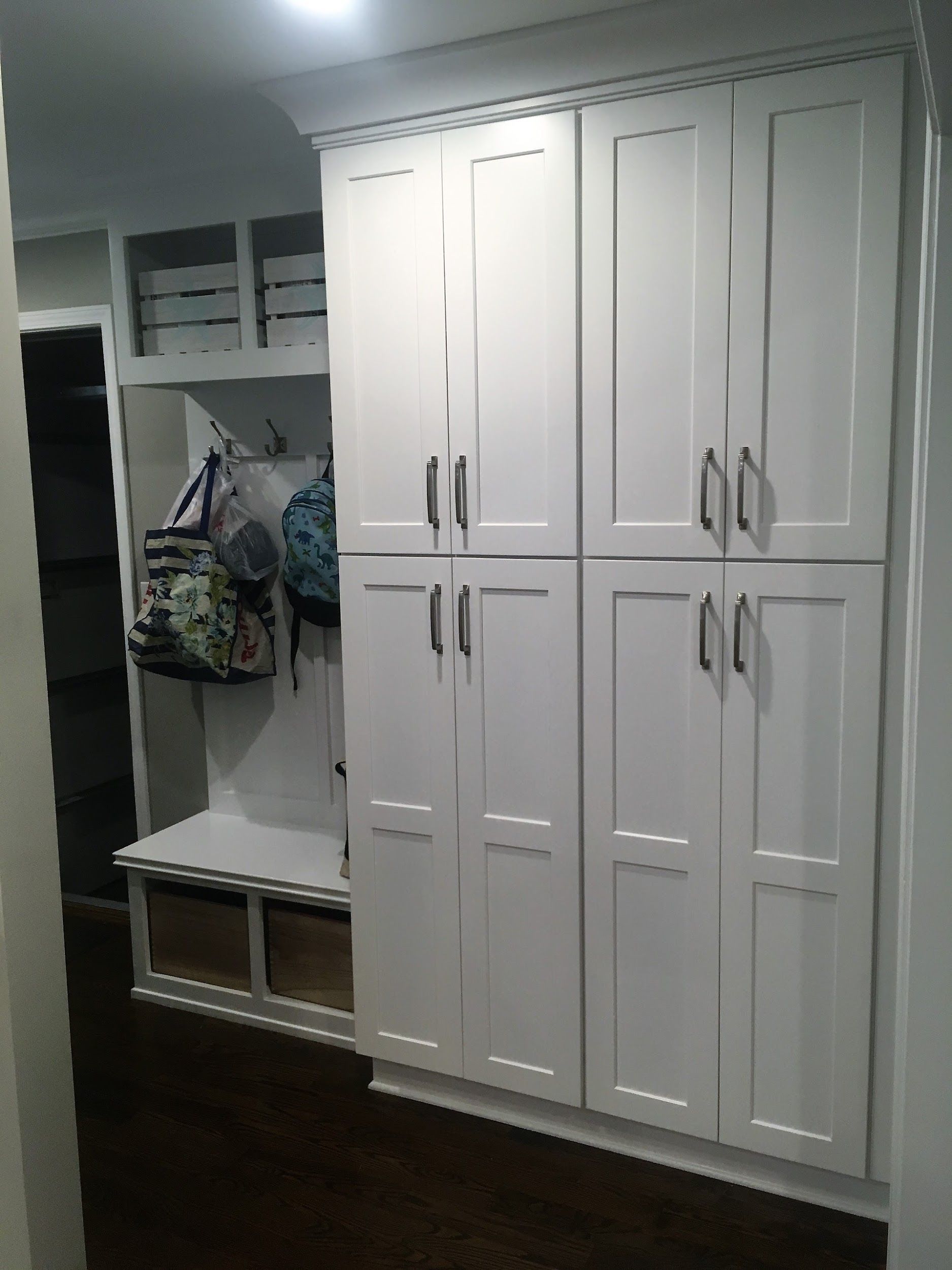 White built-in cabinets with silver handles next to a bench with coat hooks and drawers in a hallway.
