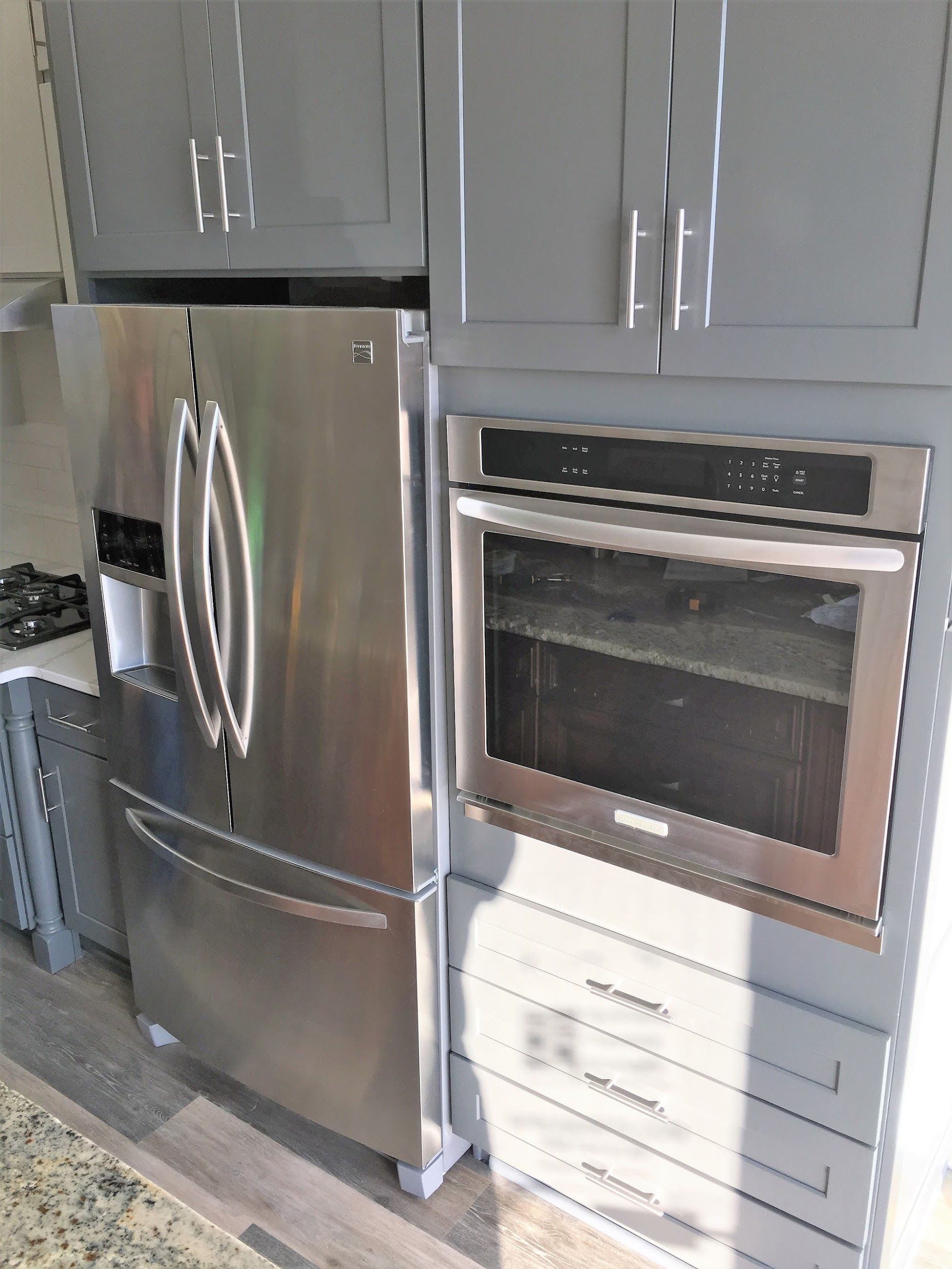 Stainless steel refrigerator and oven built into gray cabinets.
