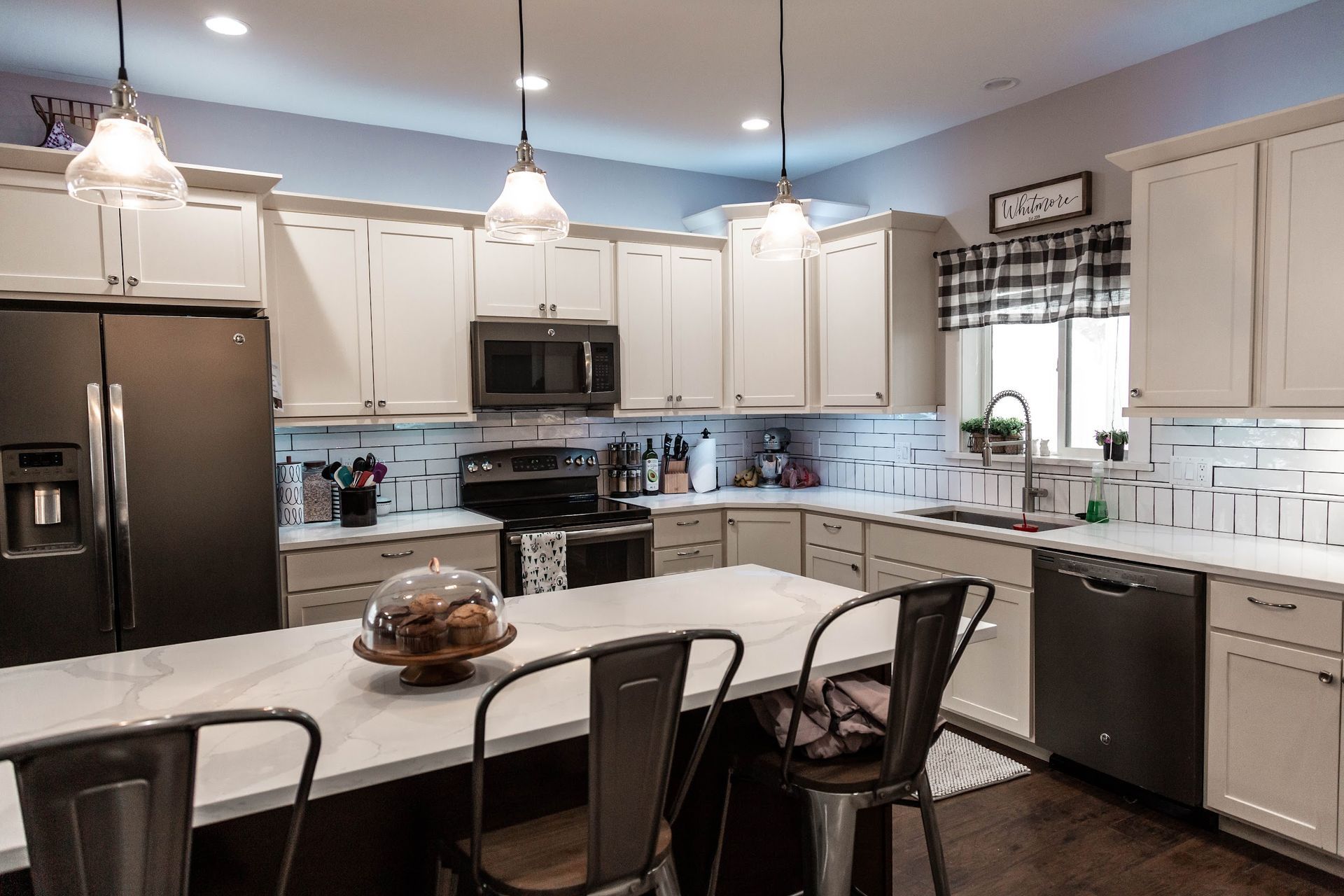 Kitchen with island, white cabinets, dark appliances, and pendant lights.