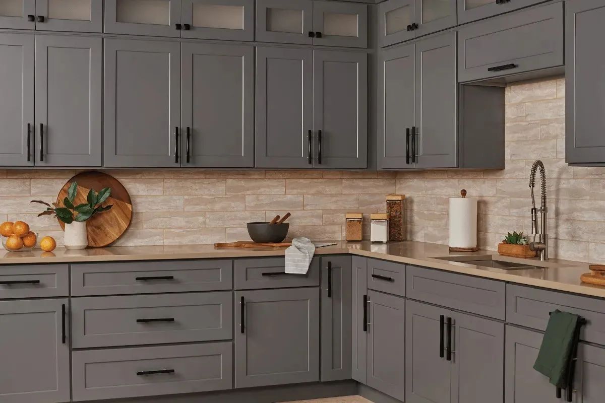 Gray kitchen cabinets with black hardware and light-colored countertops.