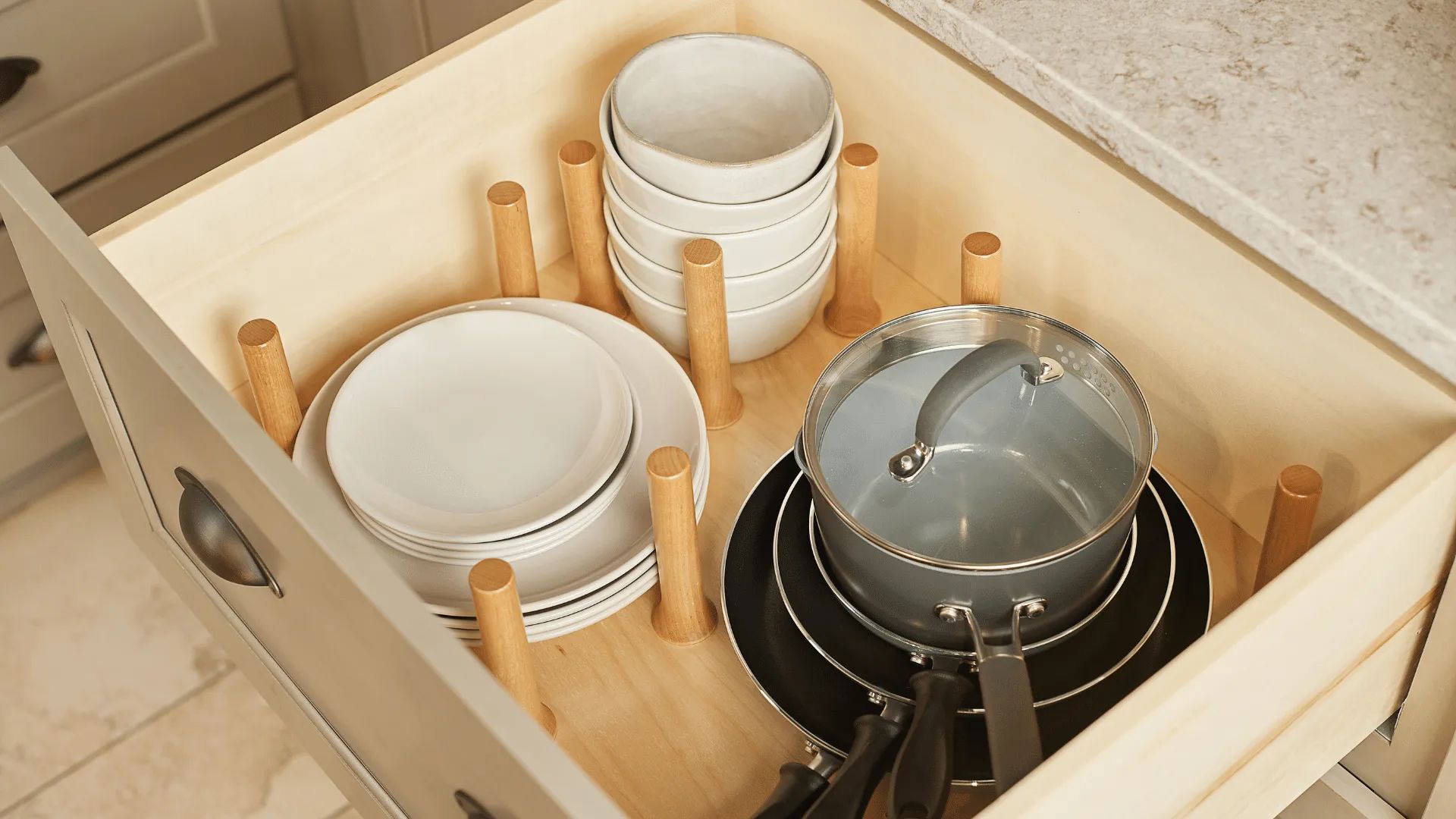 Kitchen drawer organized with plates, bowls, and pots separated by wooden pegs.