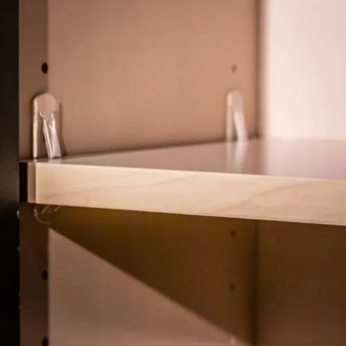 A close-up of a shelf held up by clear plastic shelf supports inside of a cabinet.