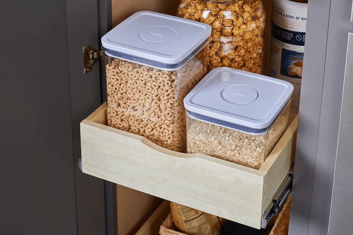 A pull-out cabinet shelf holding two clear containers of food with white lids and a container of popcorn.