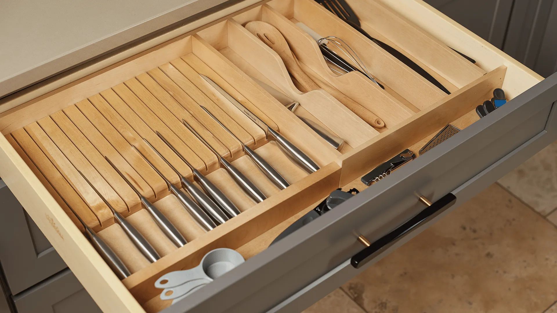 Open kitchen drawer with wooden utensil organizer holding knives, spoons, and spatulas.