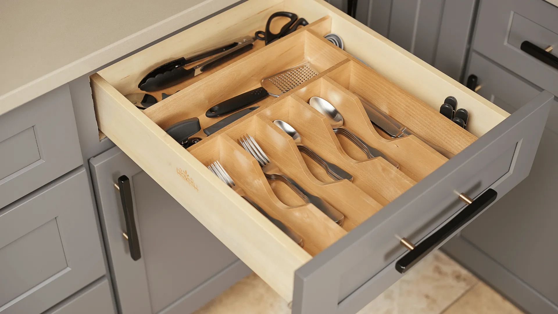 Open kitchen drawer with utensil dividers, holding silverware and kitchen tools.