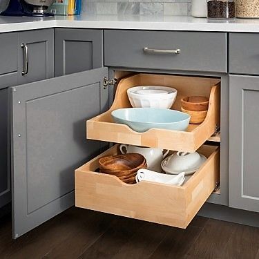 Gray kitchen cabinet with pull-out shelves holding bowls and dishes. Wooden shelves and gray cabinet.