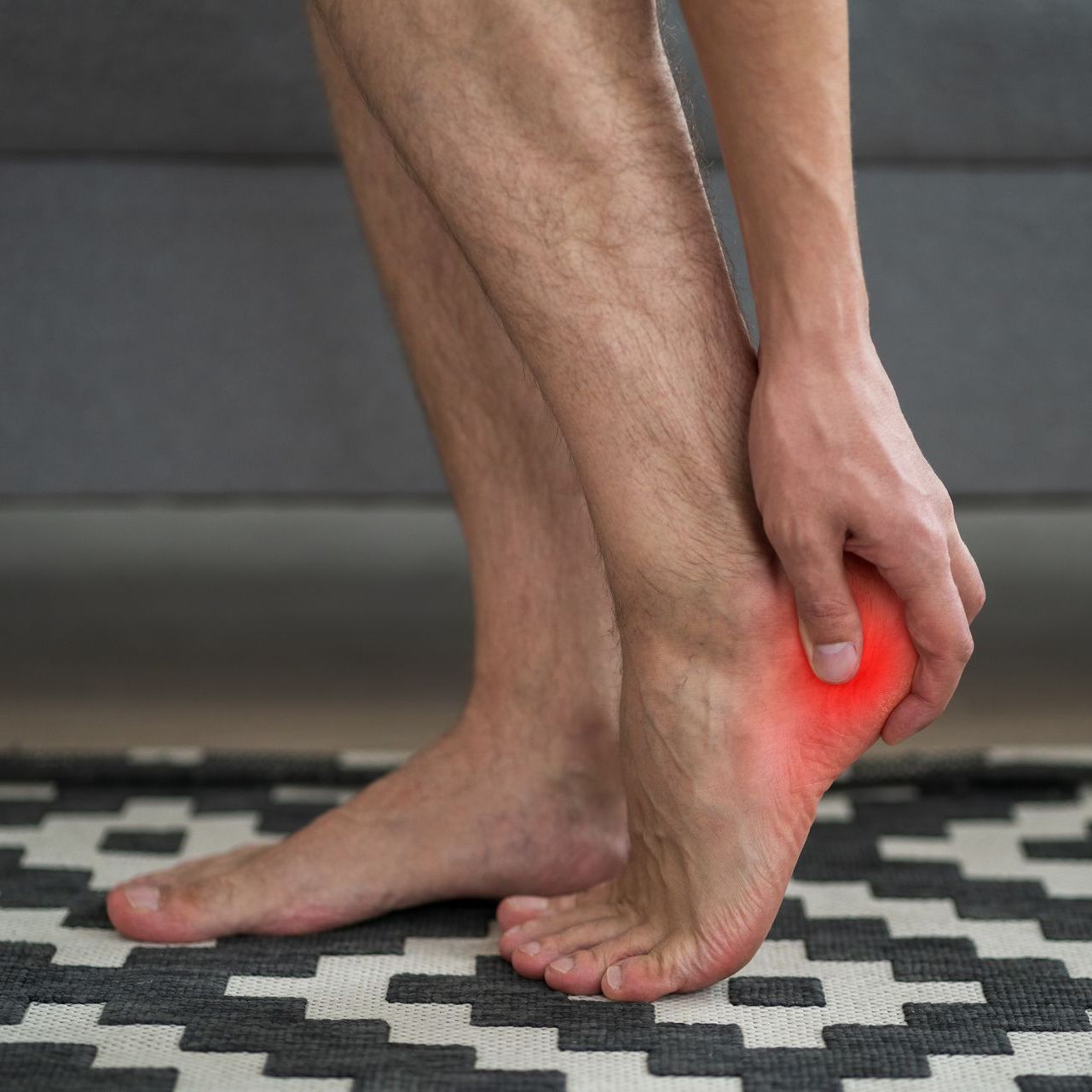A woman is holding her foot in pain while standing on a rug.