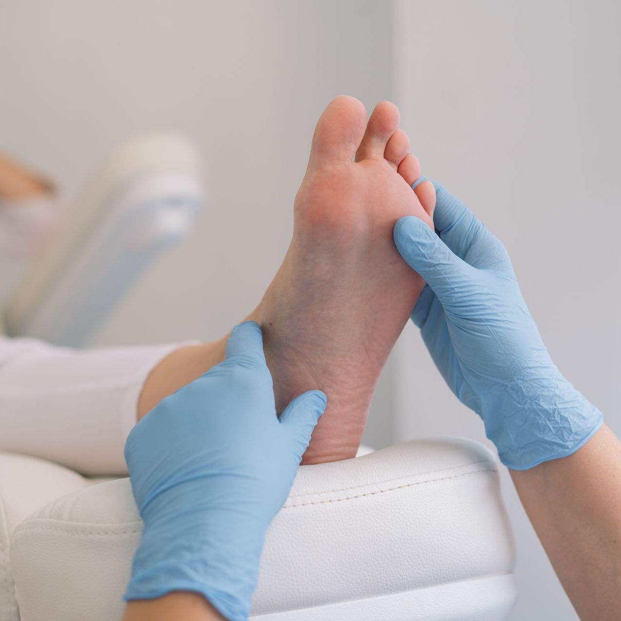 A woman in blue gloves is examining a patient 's foot.