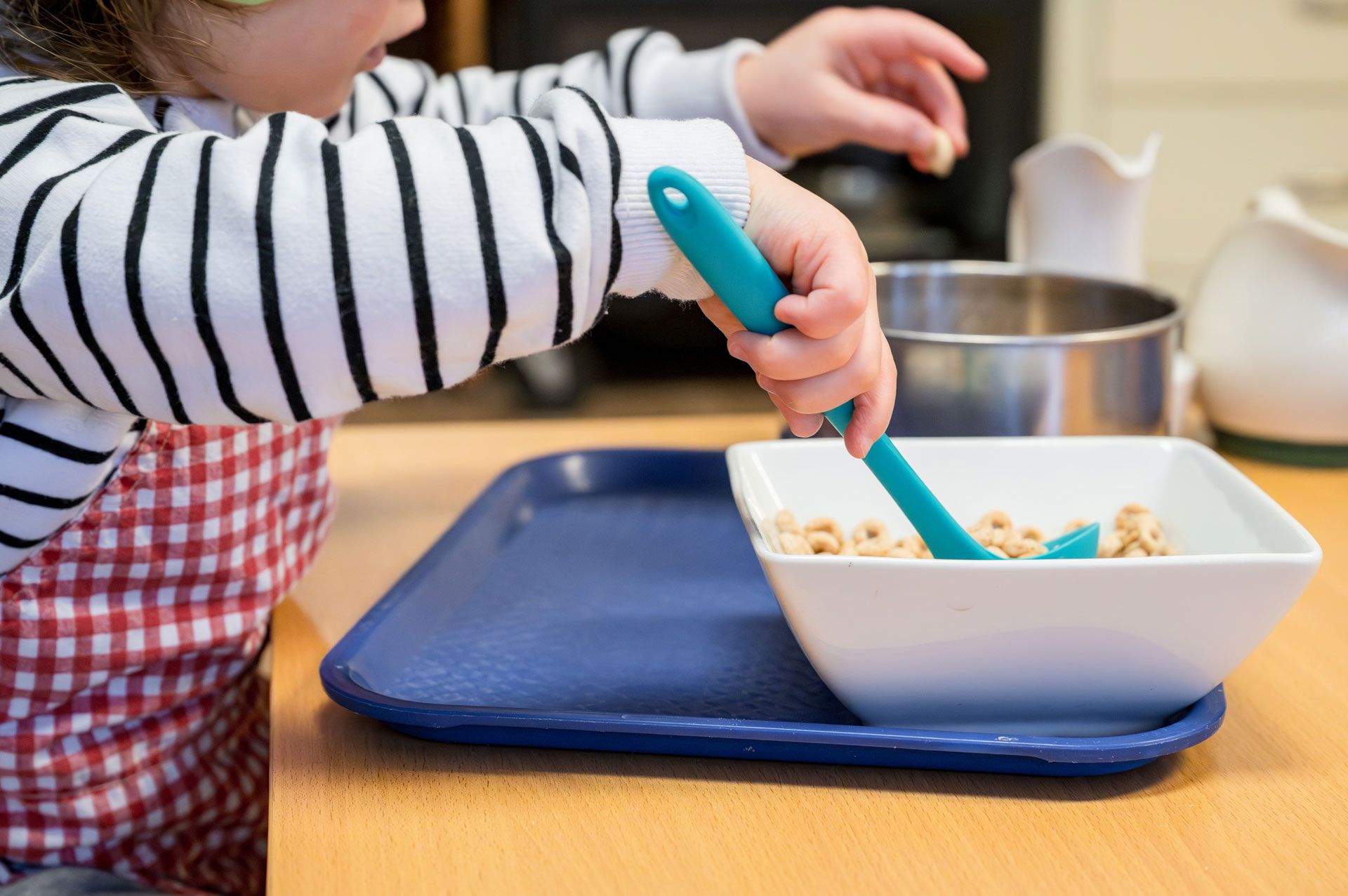 Montessori child engaged in self-feeding at a table with a spoon and bowl