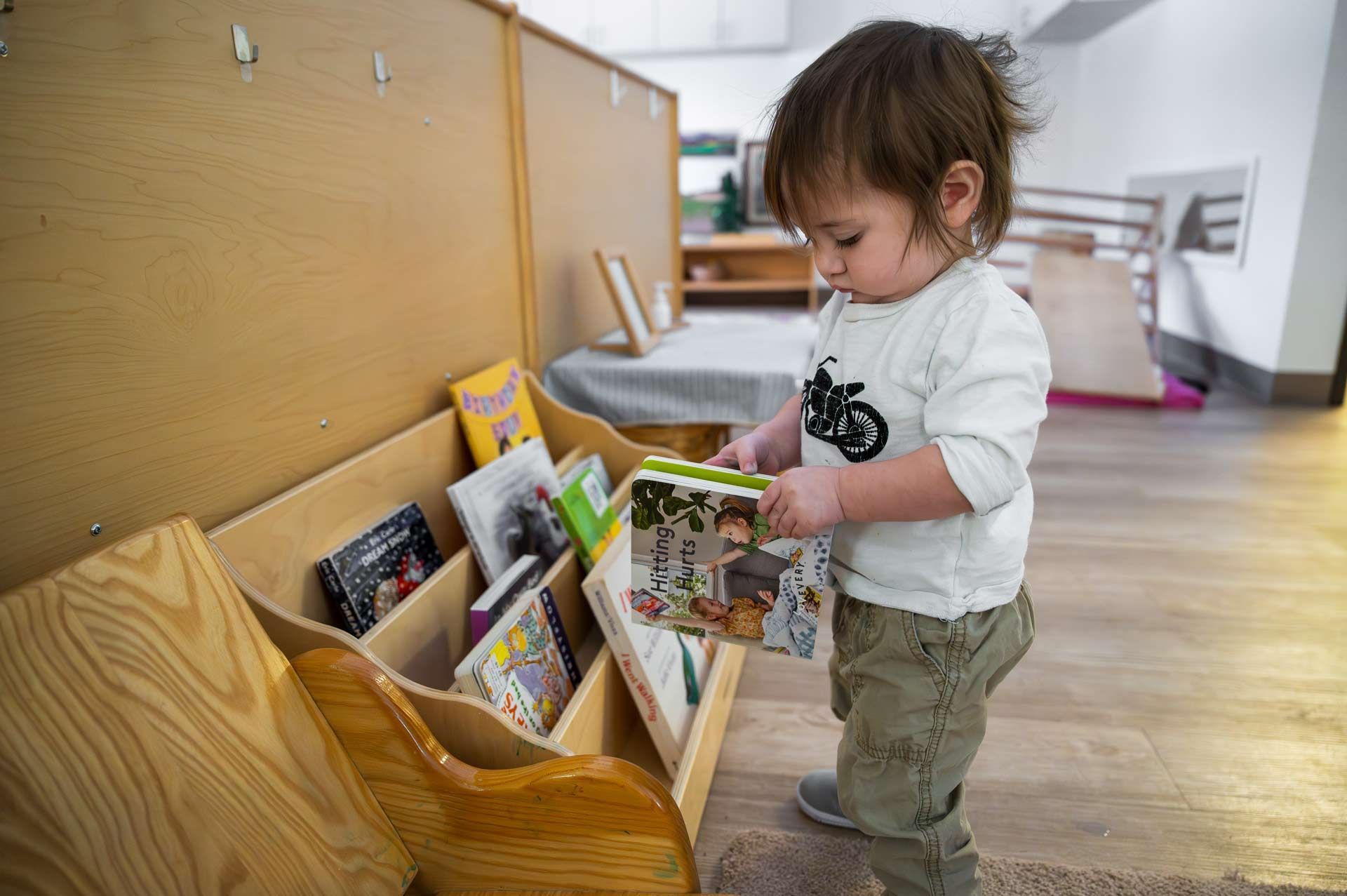 Montessori child selecting a book from a wooden bookshelf in a classroom
