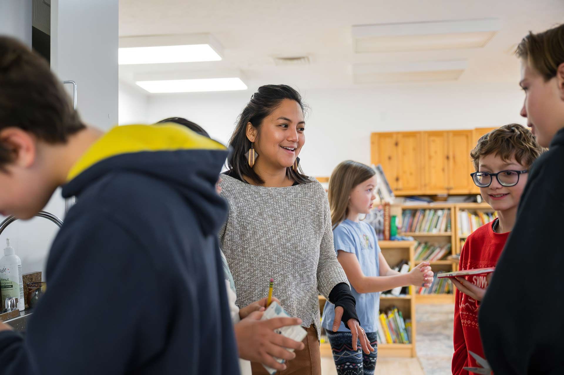 Montessori guide smiling while interacting with a group of older Montessori children in a classroom