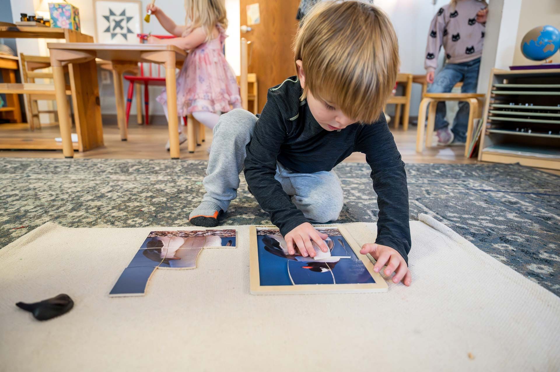 montessori child assembling a penguin puzzle on a classroom mat