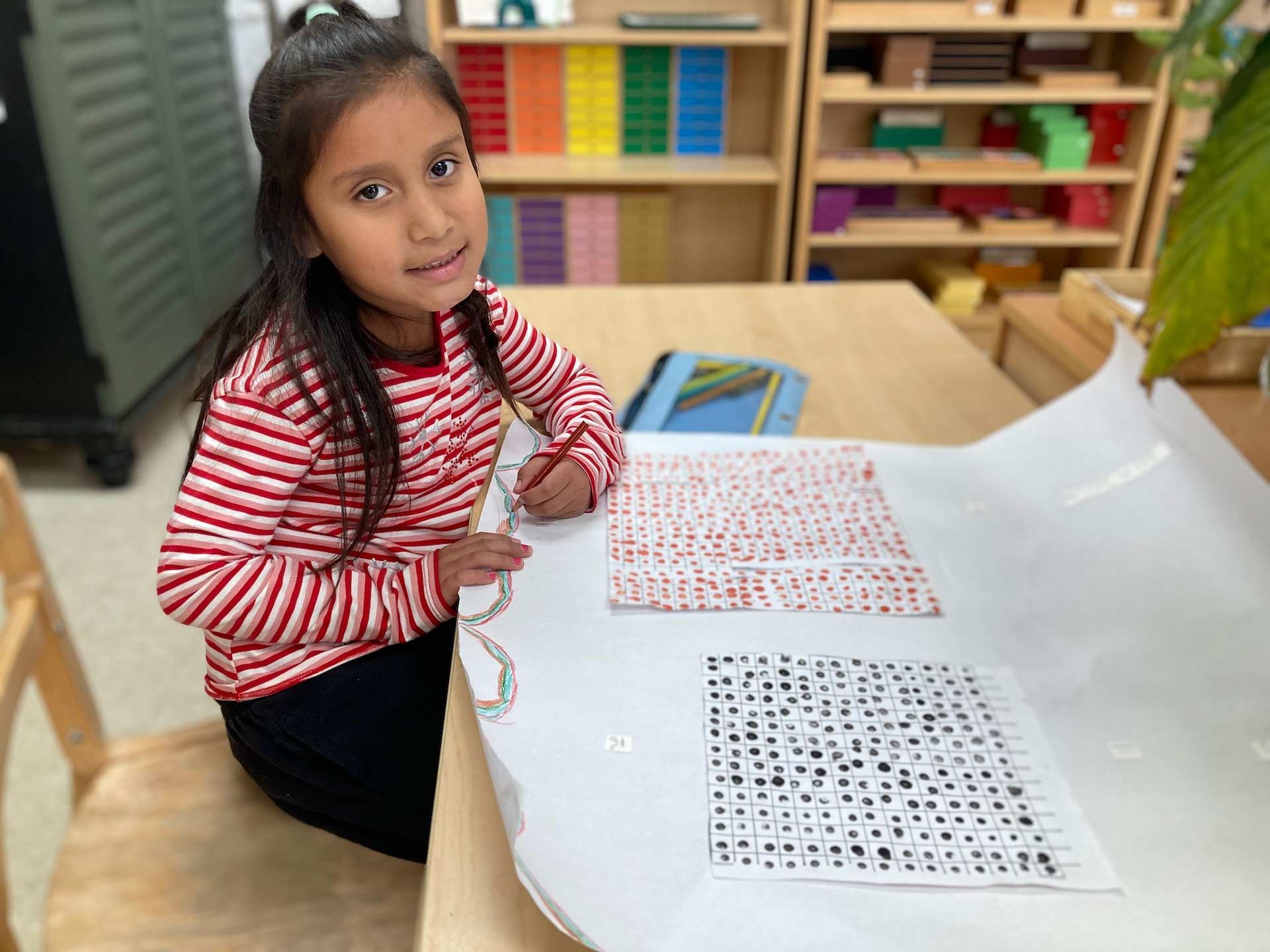montessori child drawing on paper with charts at classroom table