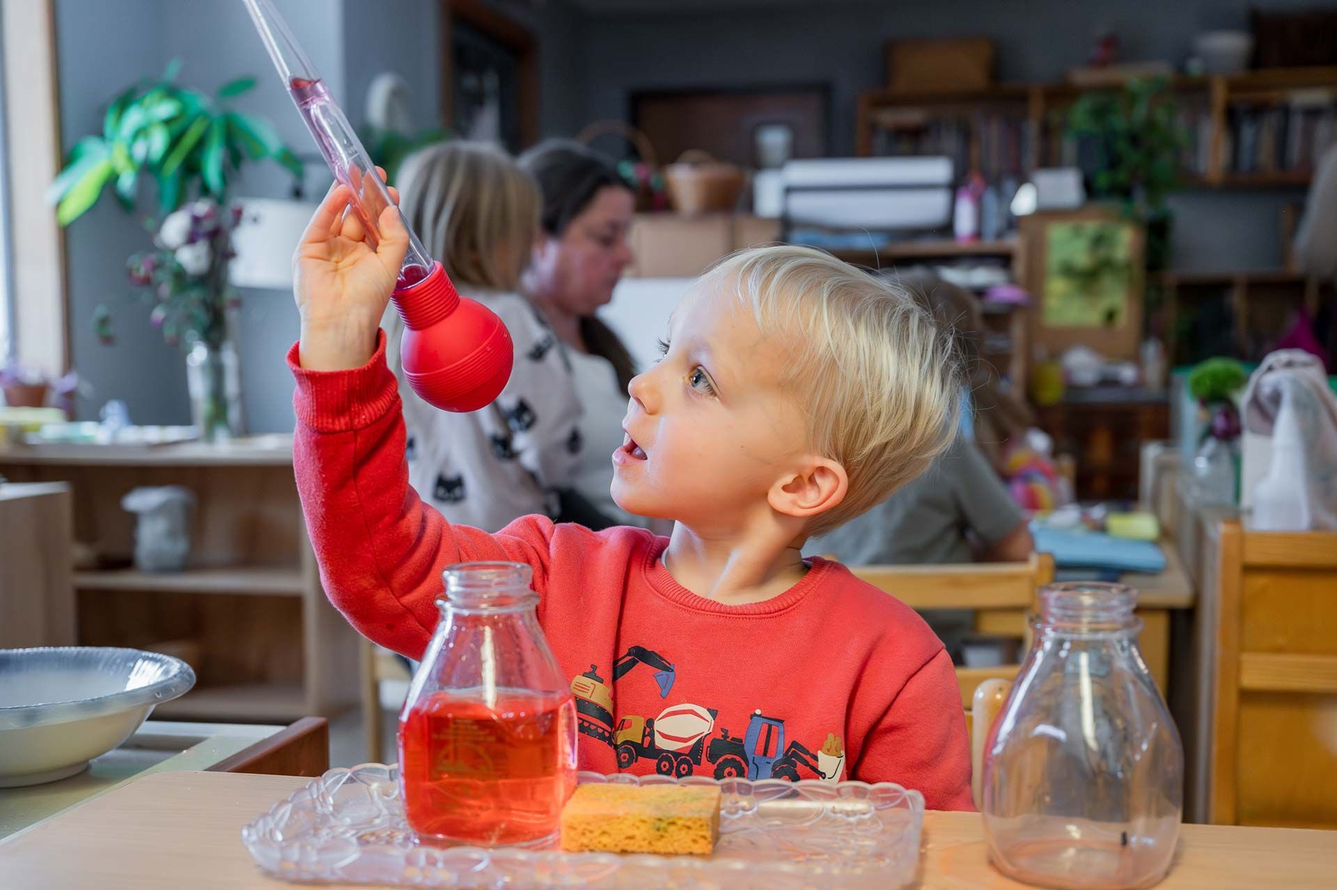 montessori child exploring liquid transfer with jars pipette and sponge in a classroom setting