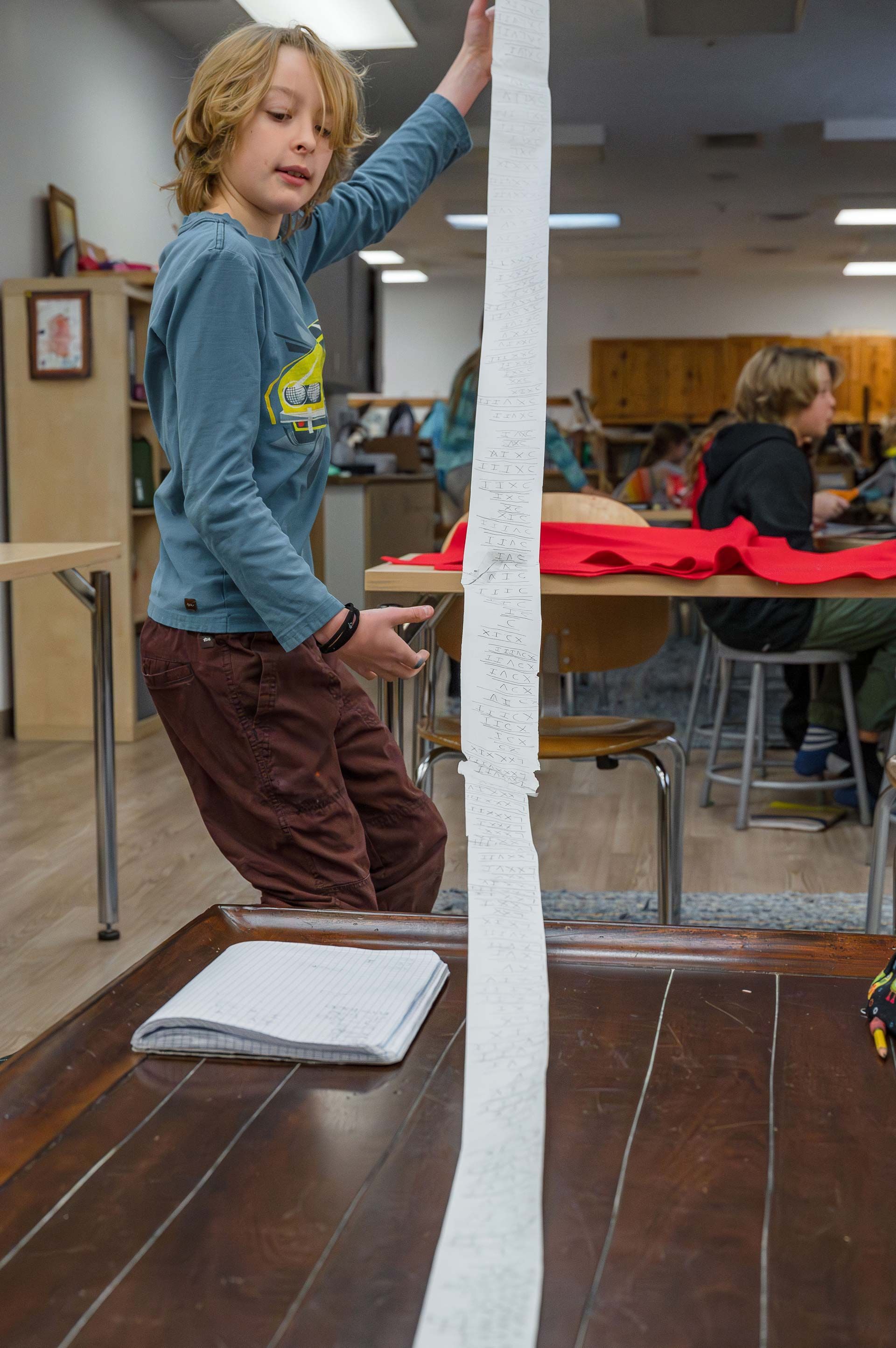 montessori child holding a long strip of math problems in a classroom setting