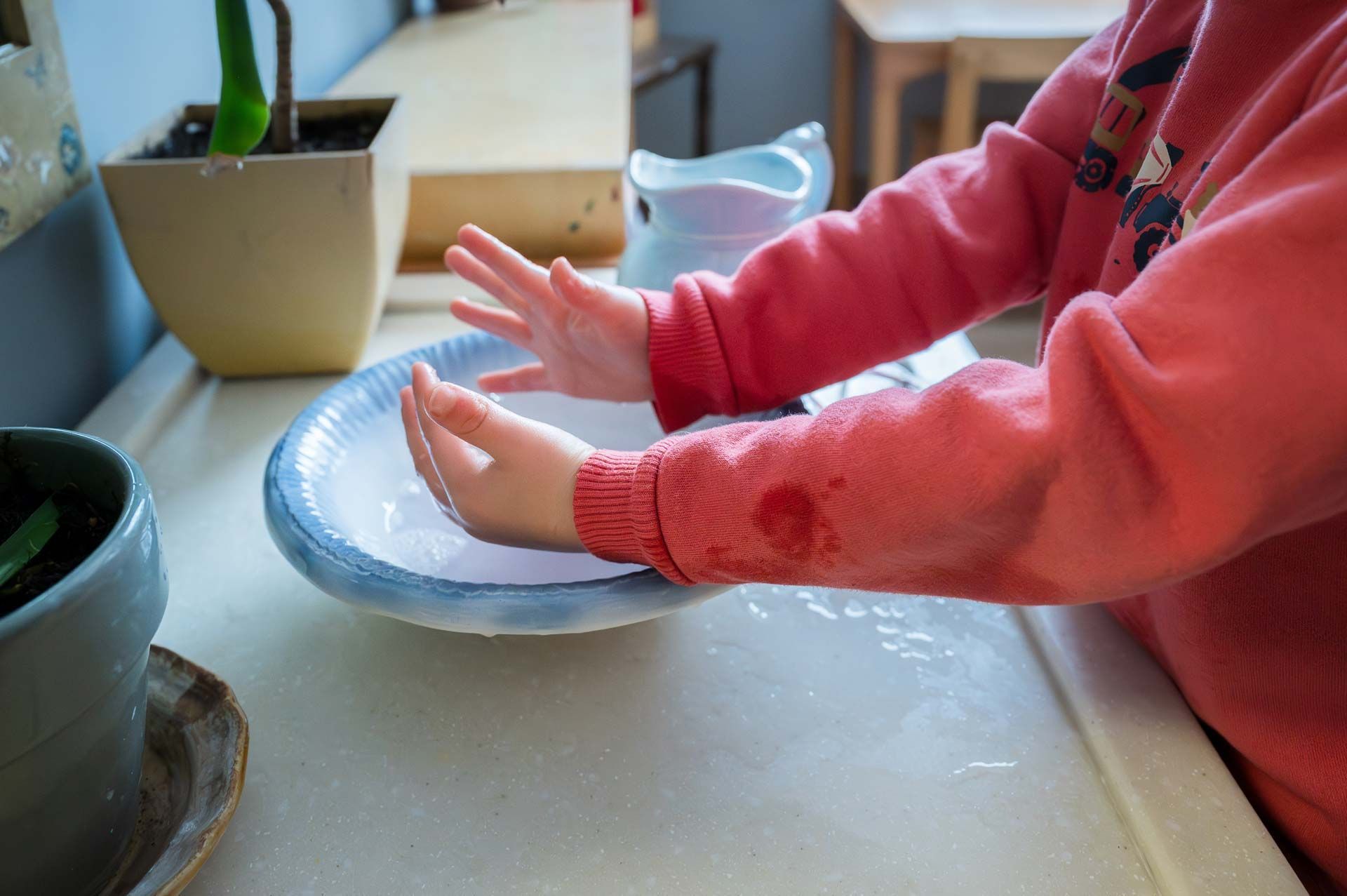montessori child in red sweatshirt washing hands in shallow bowl