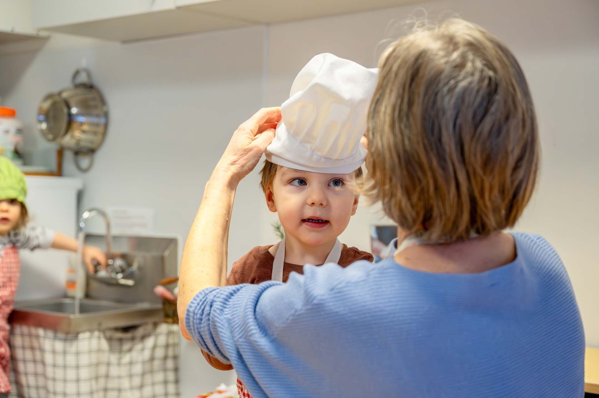 montessori child in white apron being helped with a chef's hat
