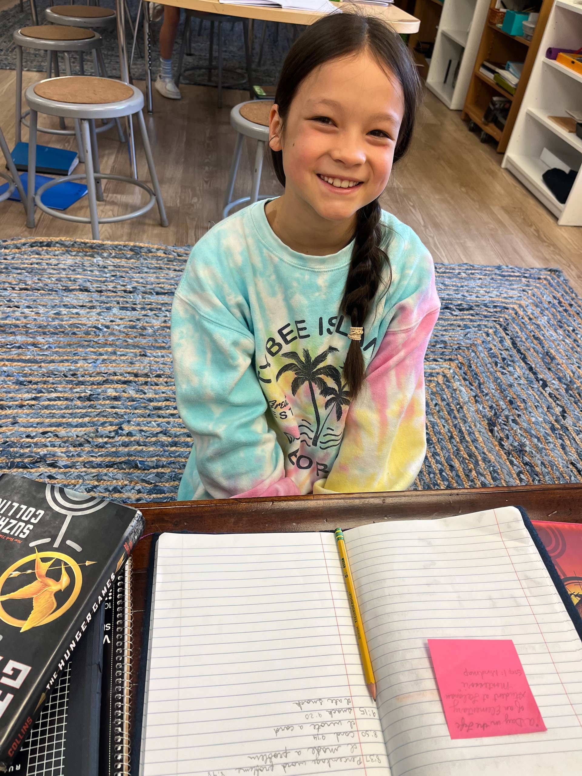 montessori child reading and writing on rug with hunger games book