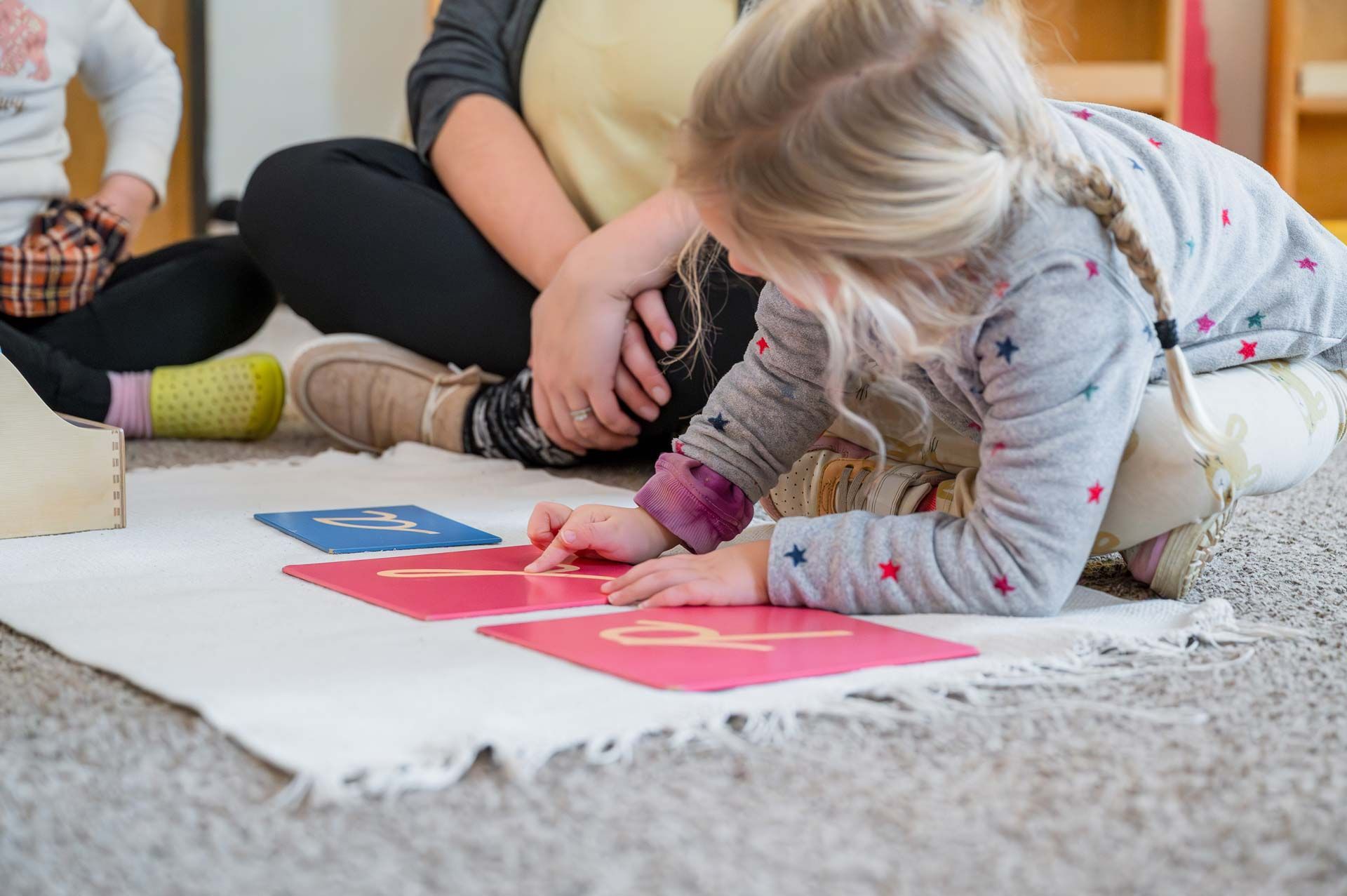 montessori child tracing sandpaper letters on a mat with guide in a classroom setting