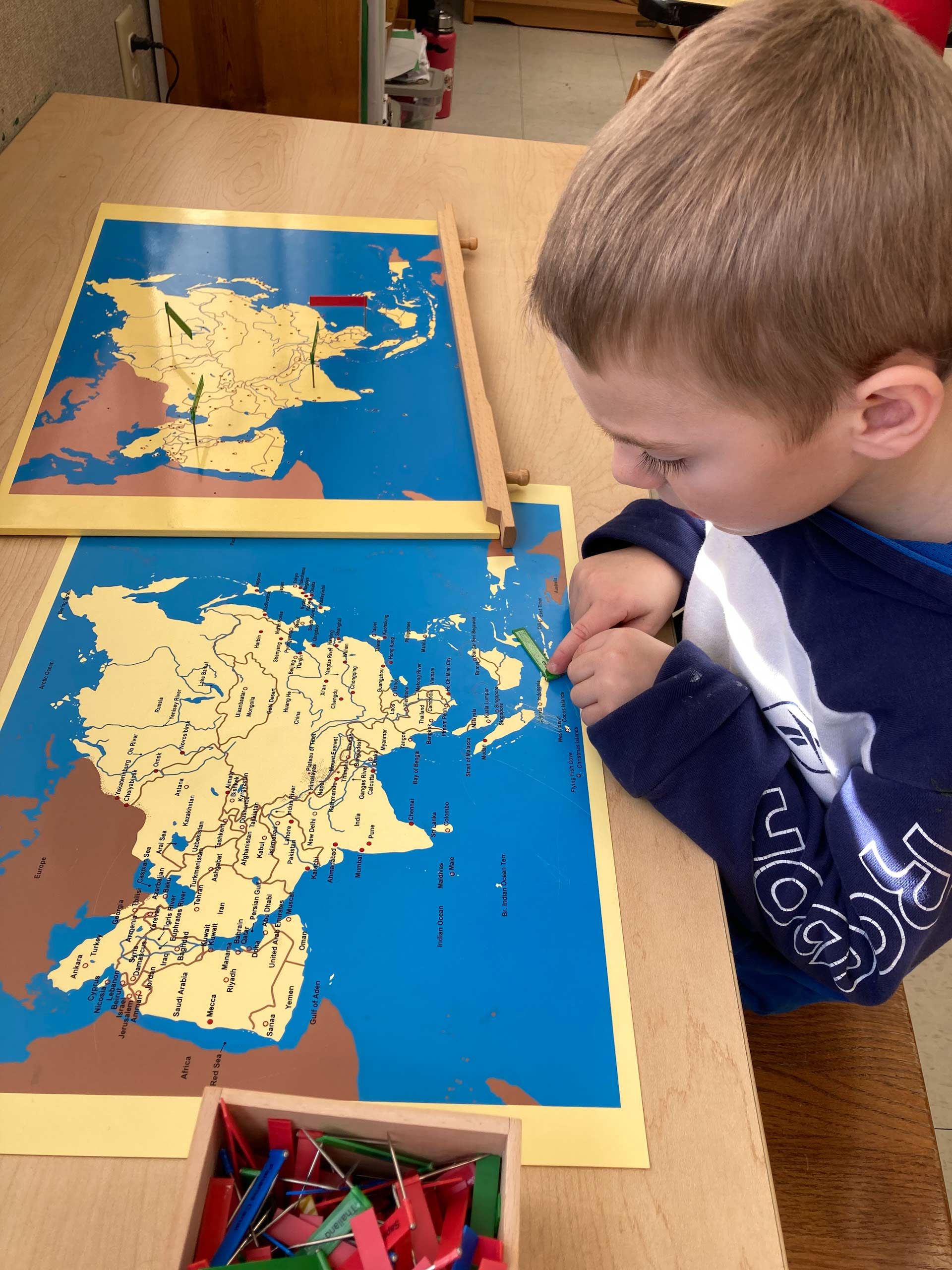 montessori child working with map of asia using pins at table