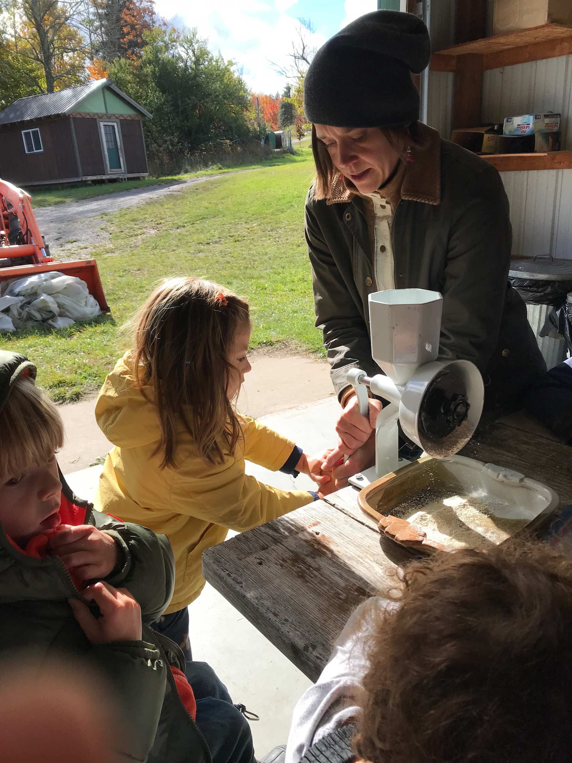 montessori children using grain grinder with guide outdoors in farm setting