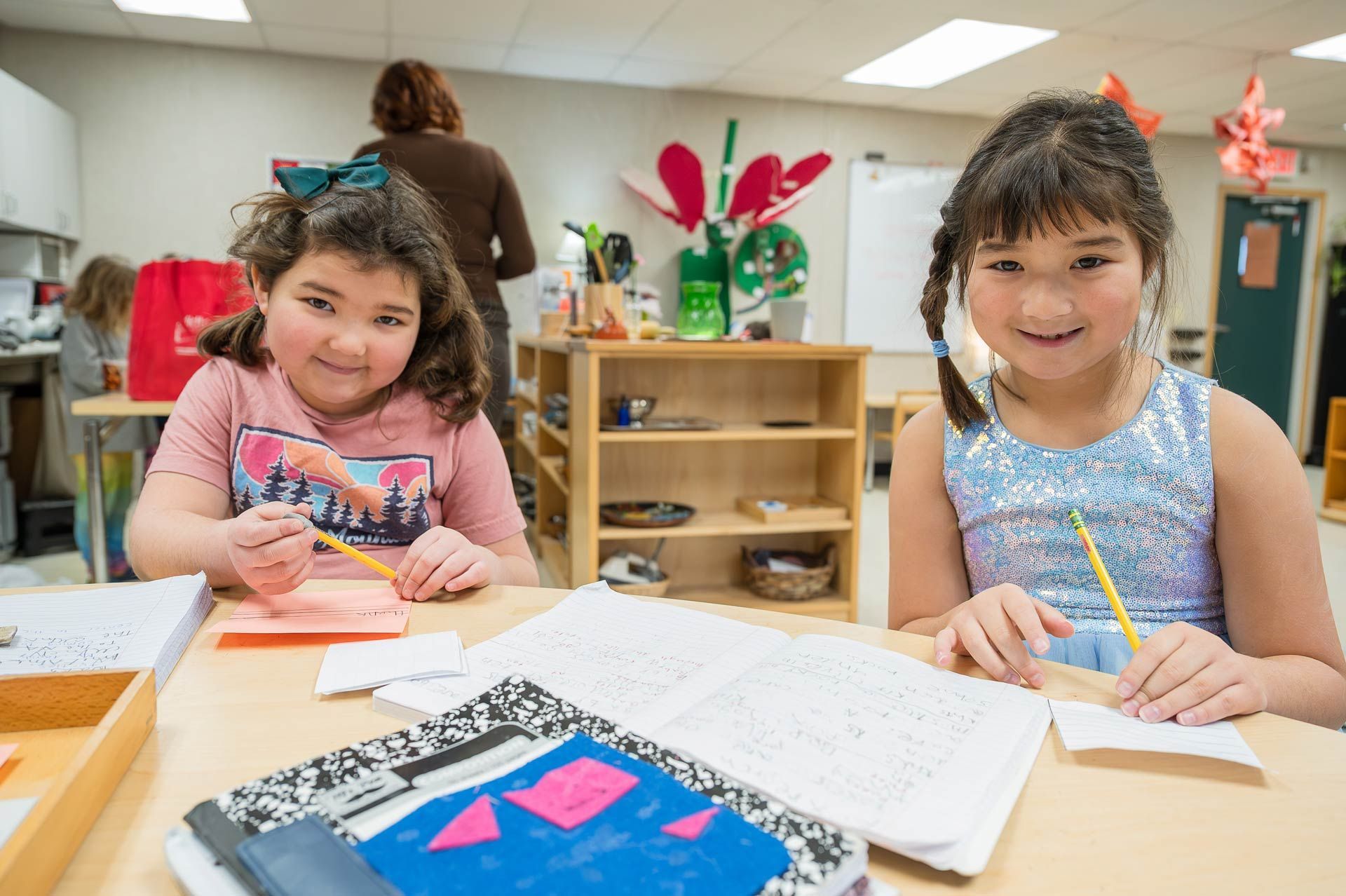 montessori children working at a classroom table with notebooks and pencils