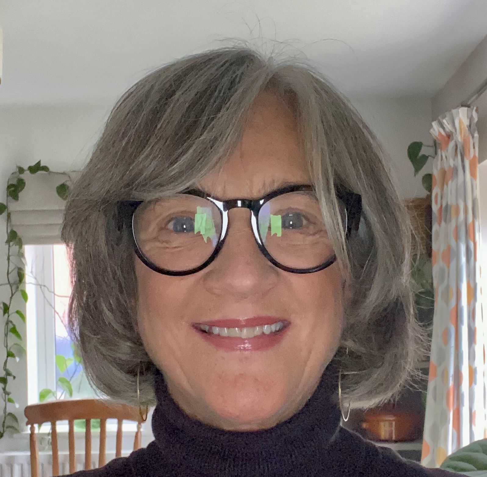 A woman wearing glasses and a black turtleneck smiles for the camera