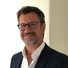 A man with a beard and glasses is wearing a suit and smiling.