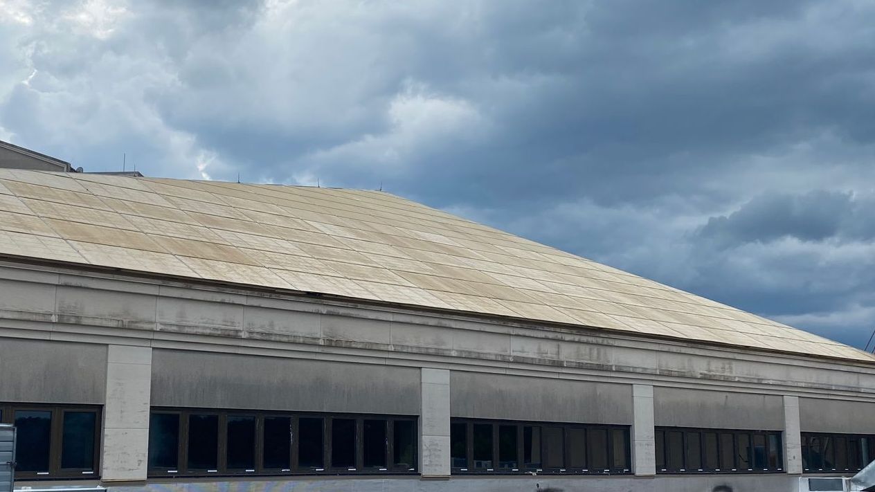 A building with a large roof and a cloudy sky in the background.