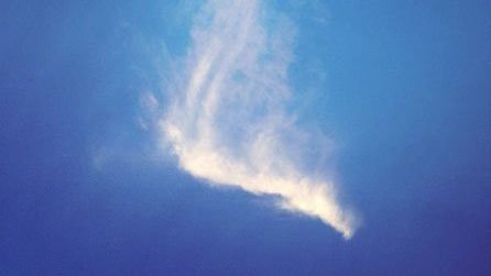 A white cloud in the shape of an angel is flying through a blue sky.