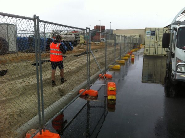 A man in an orange vest is standing next to a chain link fence