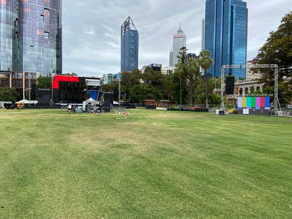 A large lawn with a stage in the middle of it in front of a city skyline.