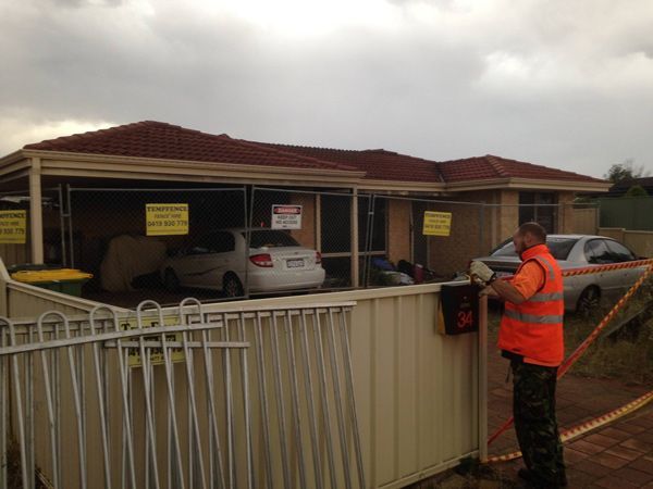 A man in an orange vest is working on a fence in front of a house.