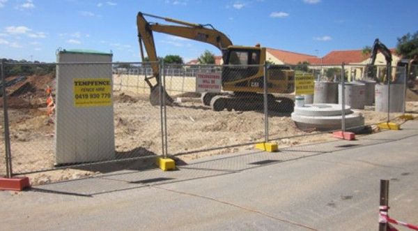 An excavator is working on a construction site behind a fence.