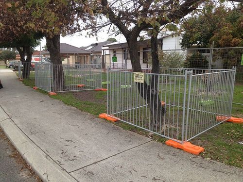 A metal fence is surrounding a grassy area next to a sidewalk.