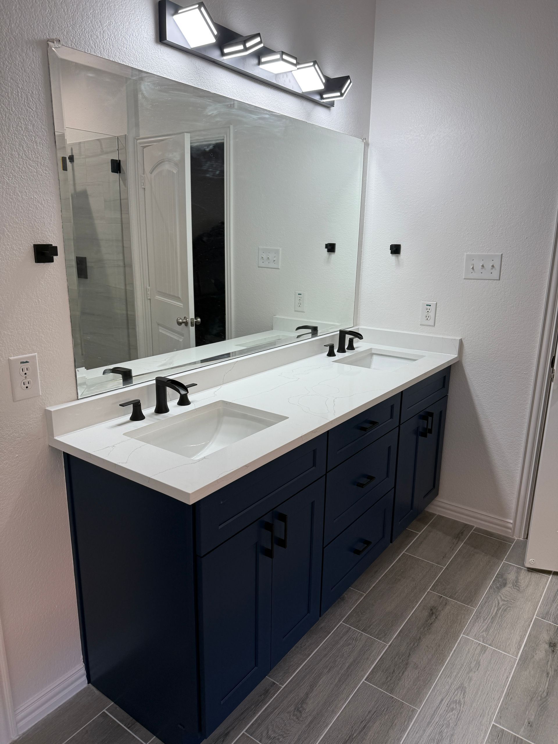 A double vanity with a white countertop and navy cabinets, featuring a large mirror and modern lighting in a bathroom.