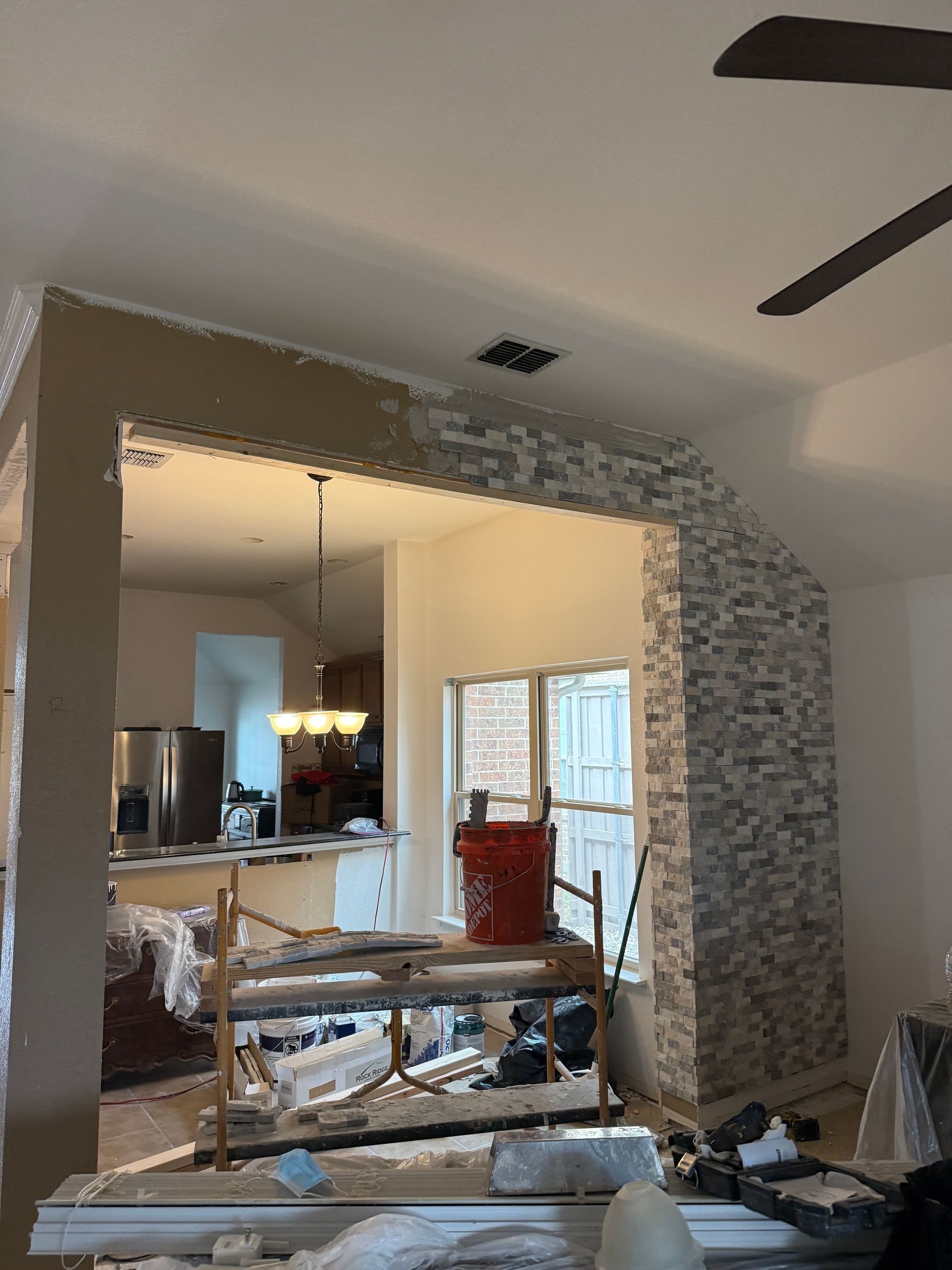 Interior of a room under renovation featuring a large, partial stone-tiled archway leading to a kitchen.