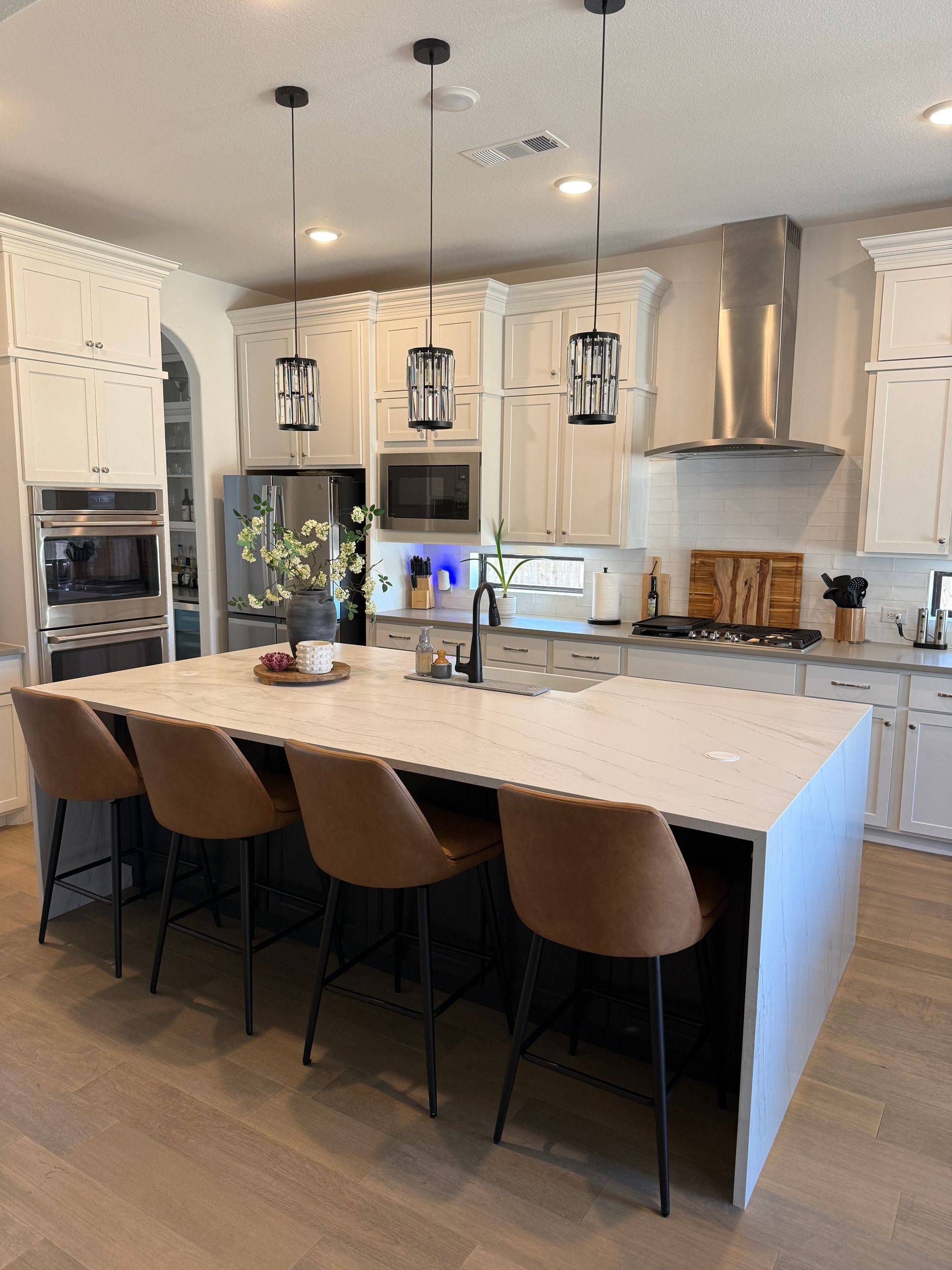 Modern kitchen with a white quartz island, four tan barstools, cream cabinetry, stainless appliances, and pendant lights.