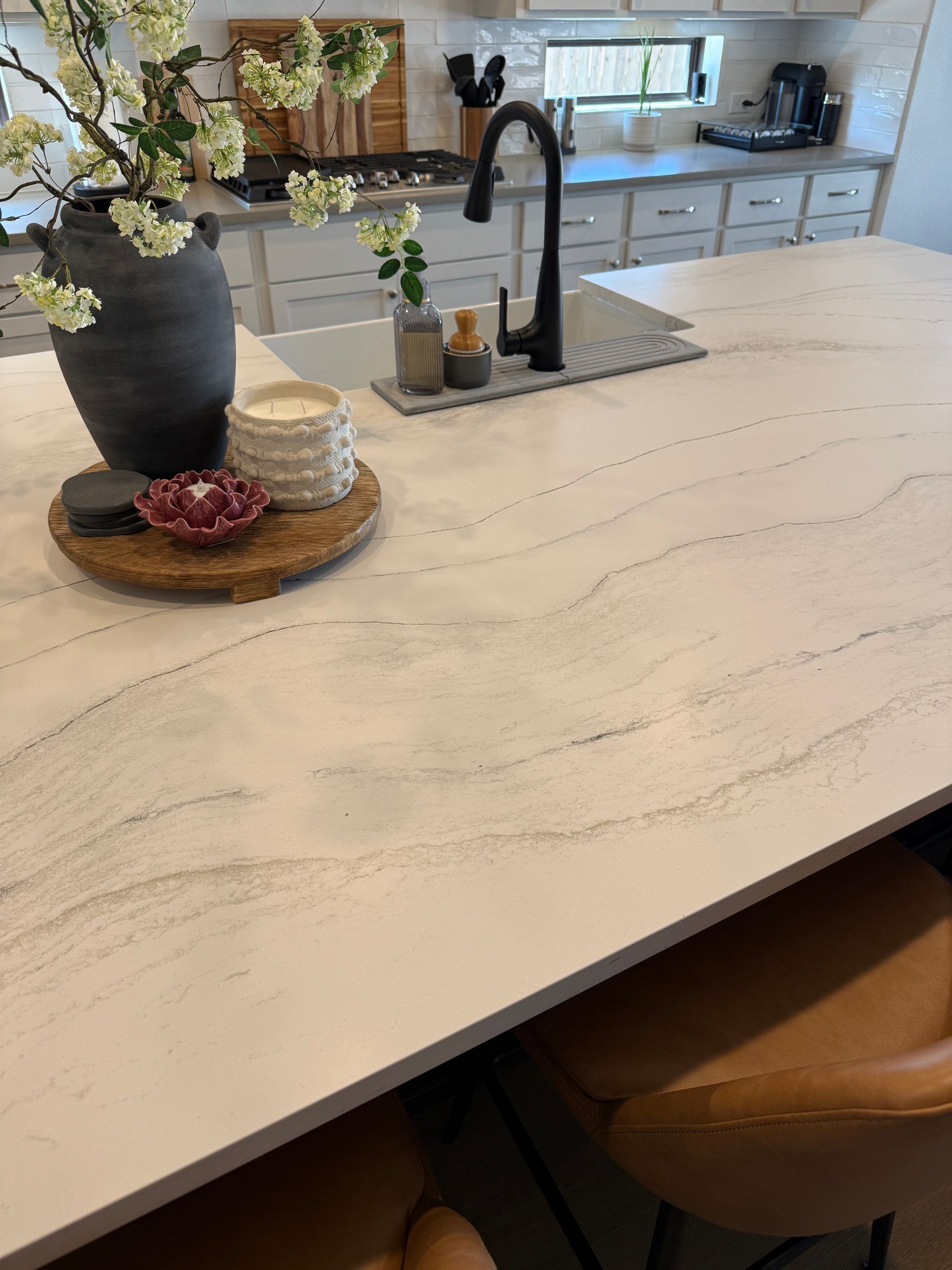 A kitchen island featuring a white quartz countertop with gray veining, a dark faucet, and a decorative vase of flowers.