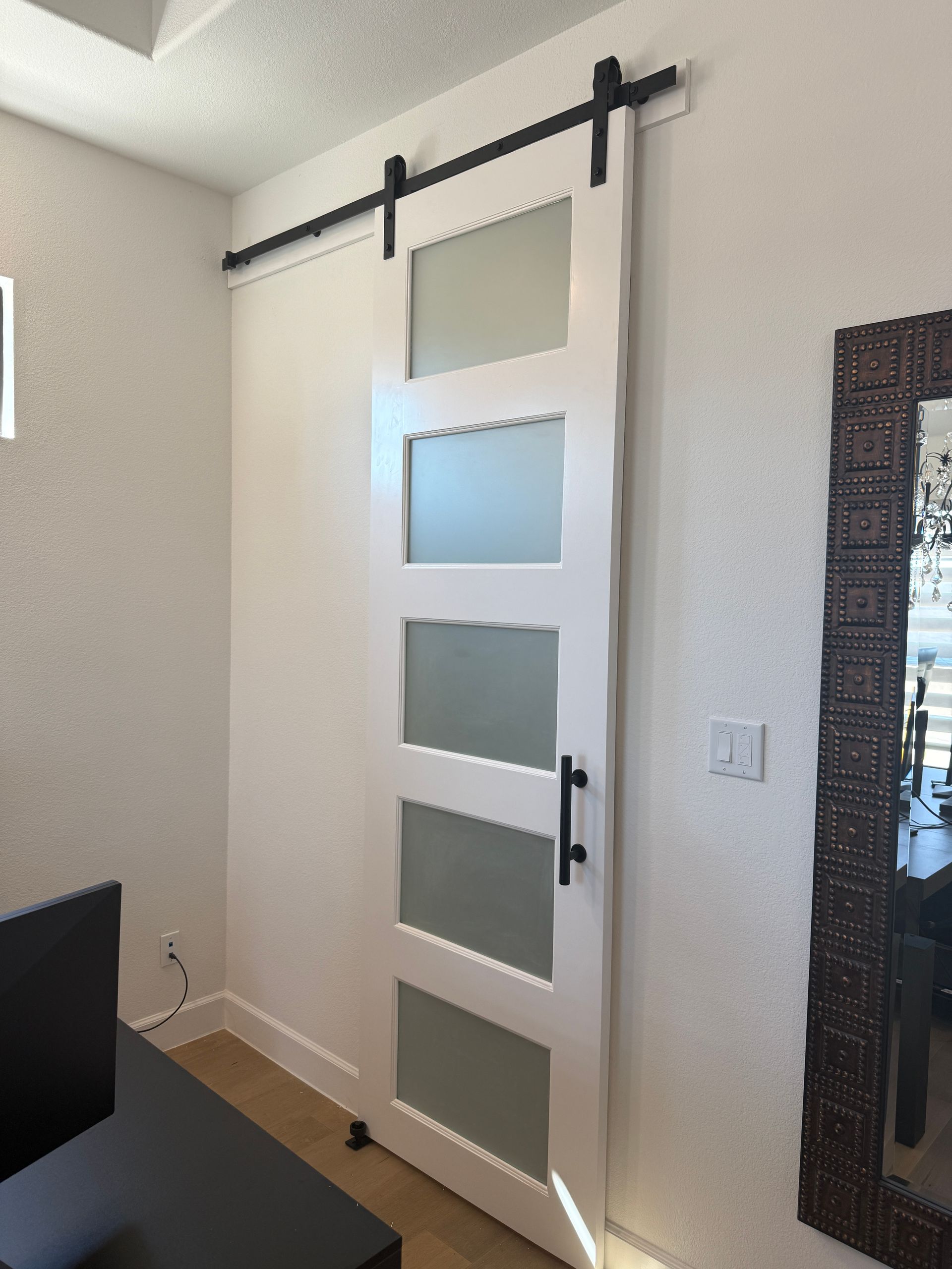A white five-panel sliding barn door with frosted glass inserts mounted on a black rail system in an interior room.