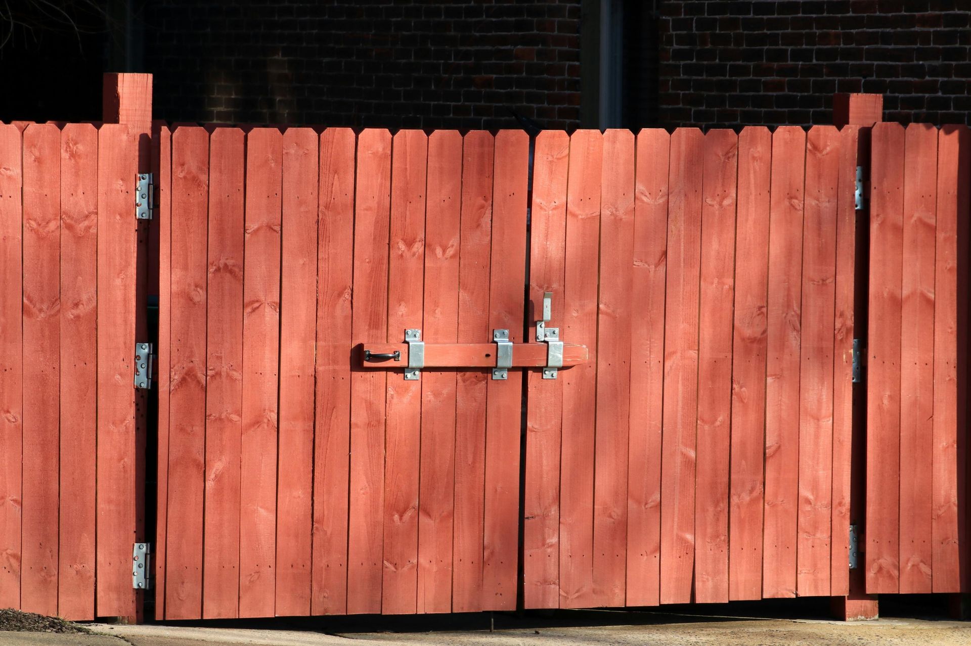 Red wooden gate with a metal latch in front of a brick building.