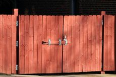 Red wooden gate with a metal latch in front of a brick building.