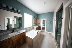 Spacious bathroom with a bathtub, two vanities, and a glass shower. Teal and wood tones.