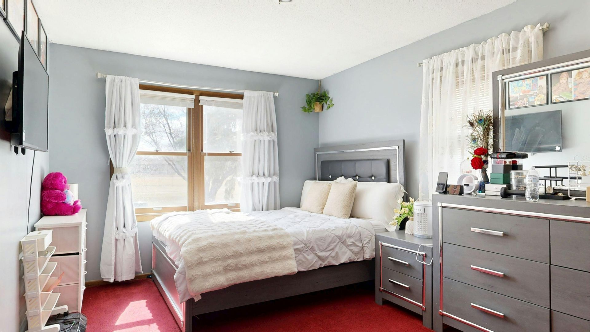 Bedroom with bed, dresser, window, and TV. Gray and white decor, red floor.