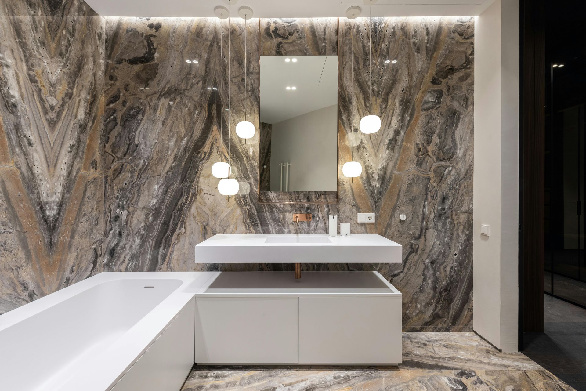 Modern bathroom with marble-effect wall, white floating vanity, rectangular mirror, and globe pendant lights.