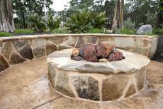 Stone fire pit with built-in seating in a backyard setting.
